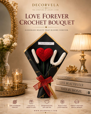 A decorative promotional image for a handmade crochet bouquet. A black wrapped bouquet with gold trim holds a red crocheted heart and white crocheted stems tied with a red ribbon, placed on a tabletop in a styled room with candles, books, and a lamp.
