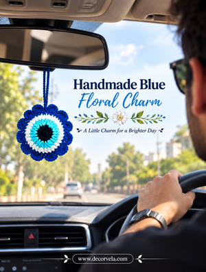 A handmade blue floral charm with a circular evil eye pattern hangs from the rearview mirror inside a car. A person is visible from behind driving the car, and promotional text reads 'Handmade Blue Floral Charm' with a website URL at the bottom.