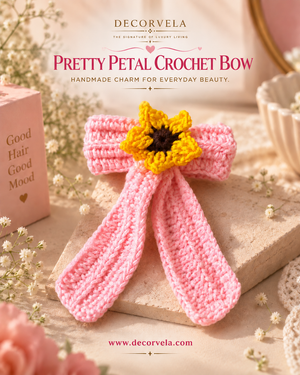 A pink crocheted petal hair bow with a yellow sunflower charm in the center, displayed on a stone surface with decorative flowers and a pink box. Decorvela branding and the text 'Pretty Petal Crochet Bow' appear in the background.