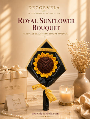 DecorVela Royal Sunflower Bouquet featuring a handmade crocheted sunflower with yellow petals and a dark brown center, wrapped in black paper with a gold ribbon, displayed on a table with a gift box, dried flowers, and a lit candle.